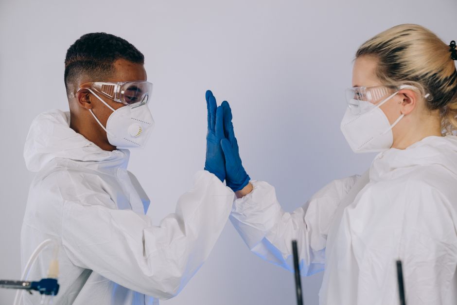 Dos profesionales de la salud con equipo de protección chocan esos cinco, promoviendo el trabajo en equipo y la protección.