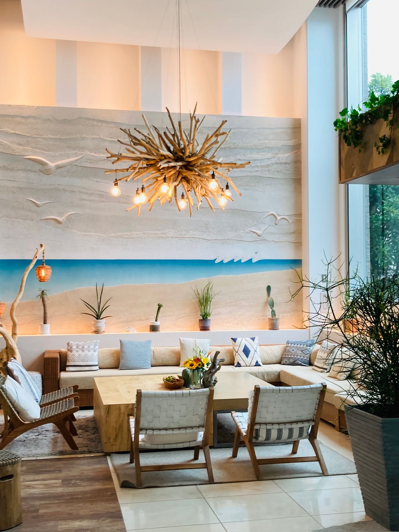 Living room with a driftwood branch chandelier, beach mural wall, and woven chairs