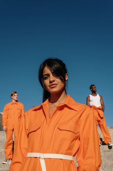 Three individuals standing outdoors in bright orange uniforms against a clear blue sky, conveying a sense of unity.