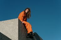 Woman in Orange Jacket Sitting on Gray Concrete Wall