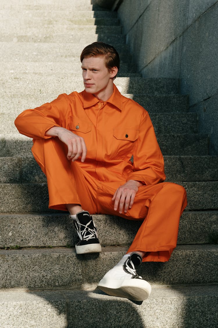 Man In Orange Coverall And Black Shoes Sitting On Stairs 