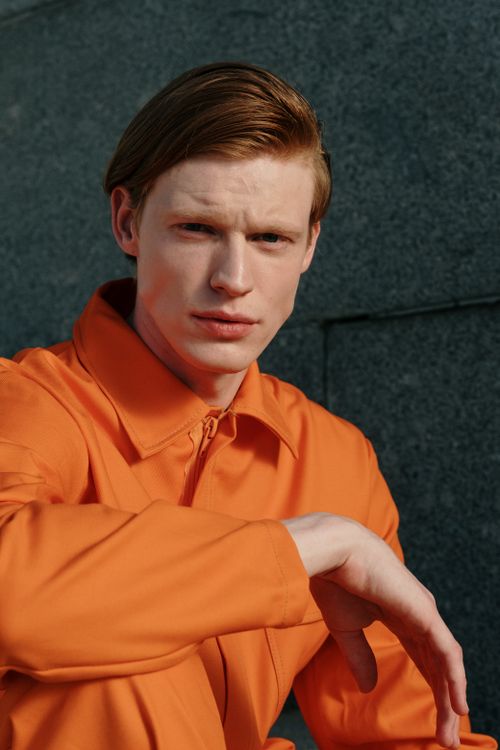 Free Striking portrait of a redhead man in an orange jumpsuit posed against a textured wall. Stock Photo