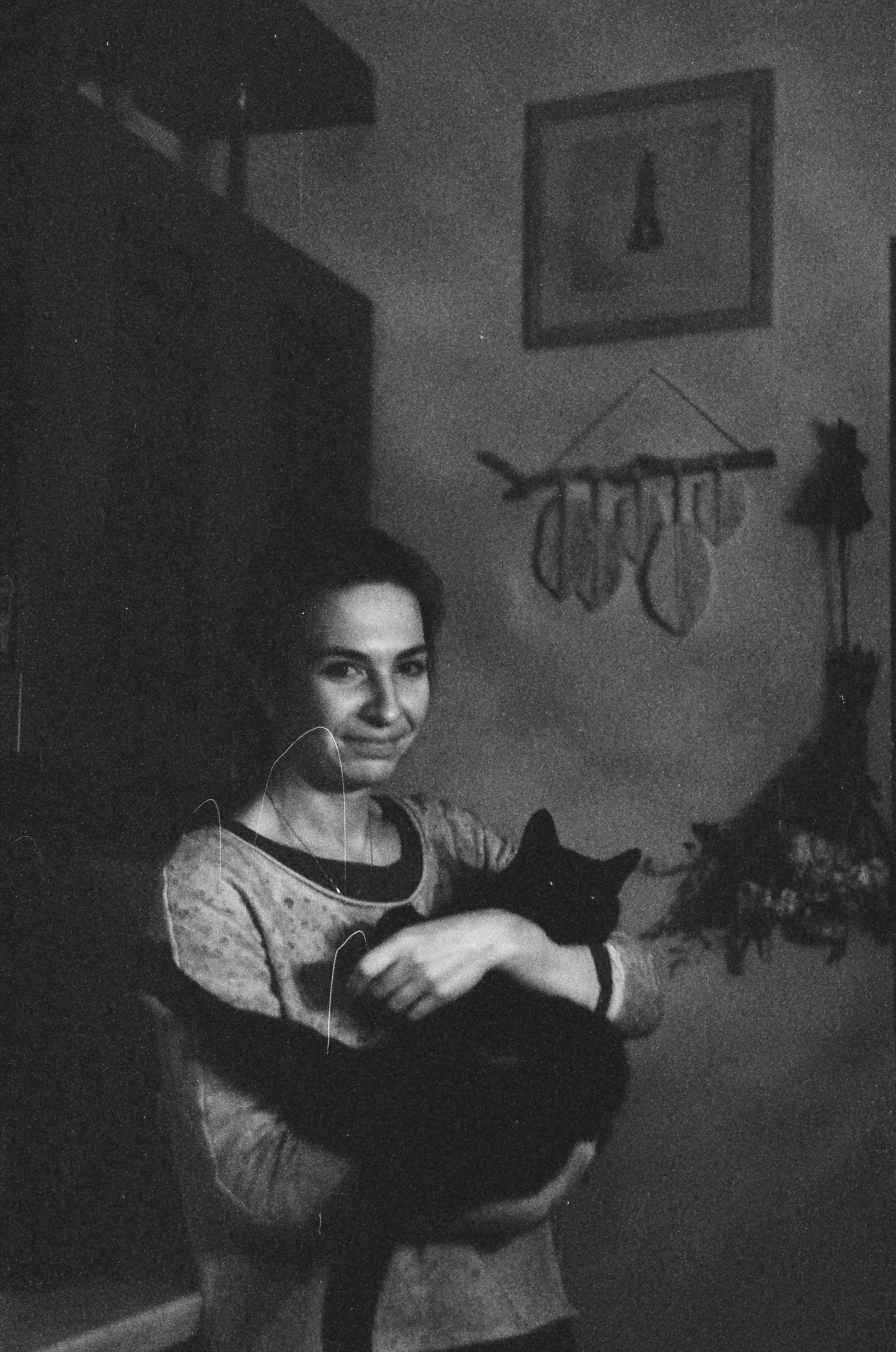A woman smiles while holding her black cat in a cozy indoor setting, captured in monochrome.