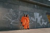 A Pair of Men Orange Jumpsuit Standing Beside Concrete Wall