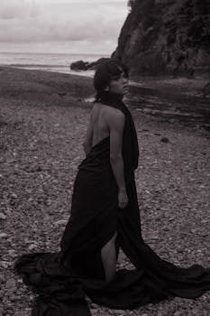 Elegant black and white portrait of a woman on a rocky beach, showcasing flowing fashion.