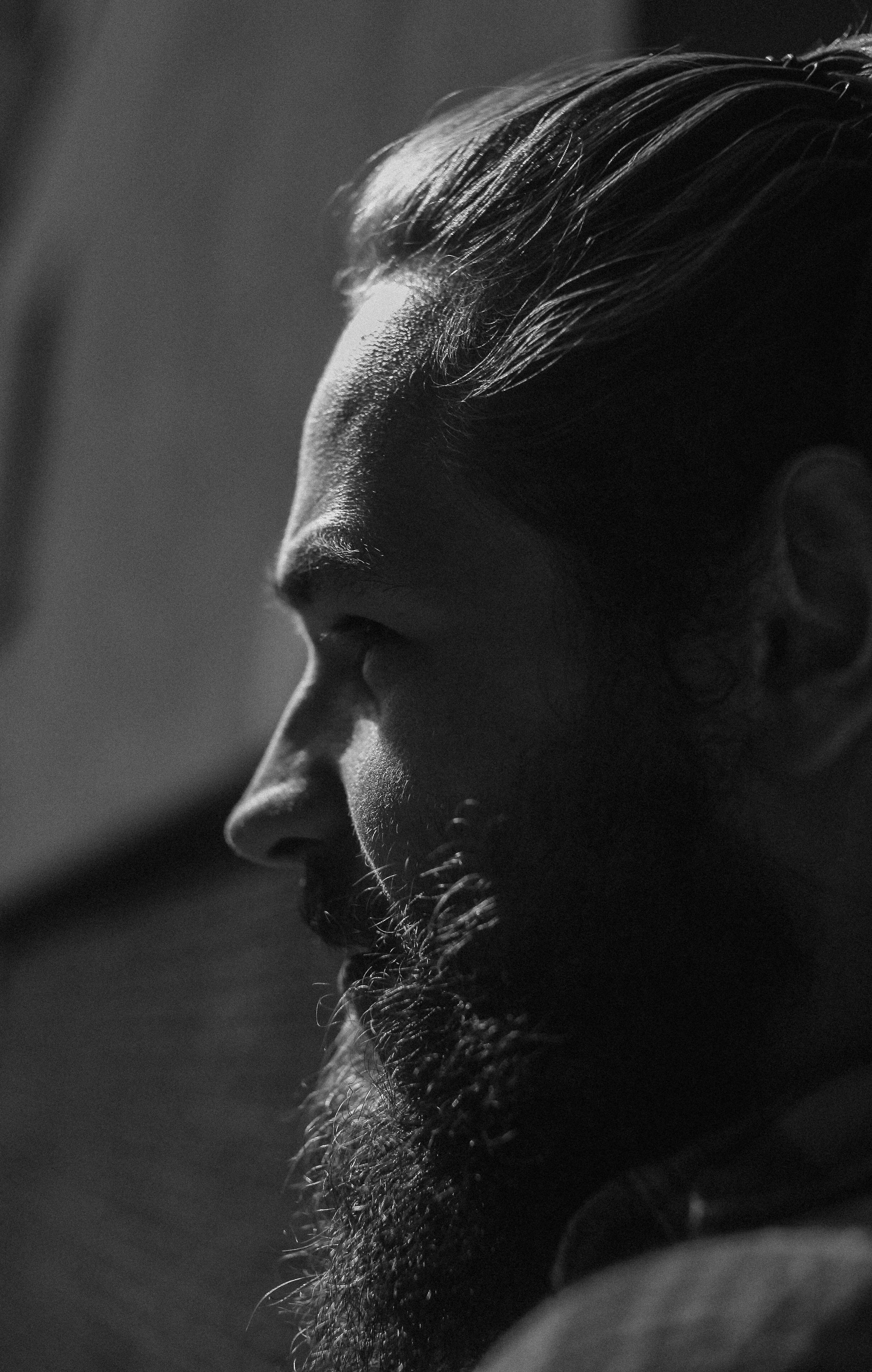 Monochrome profile of a bearded man with strong lighting and shadow contrast.