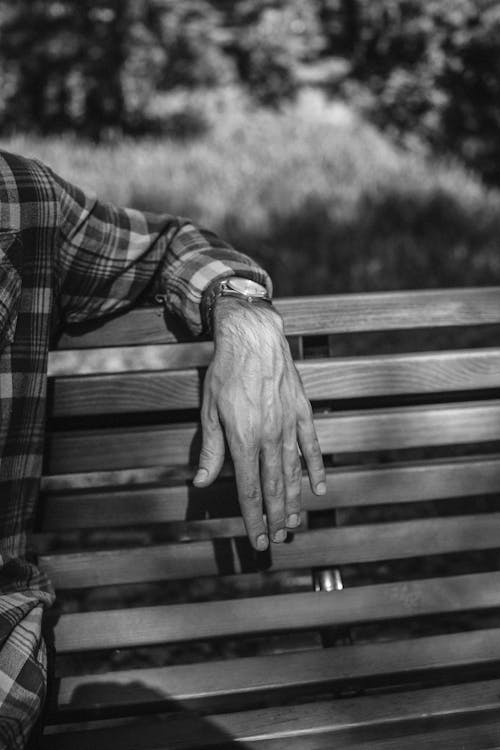 Grayscale Photo of a Person's Hand on a Wooden Bench