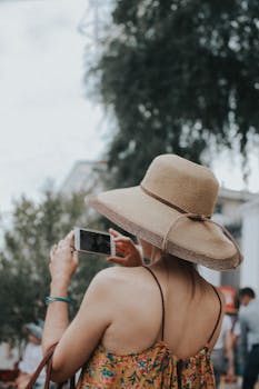 A woman in a sunhat captures a scenic outdoor view using her smartphone.