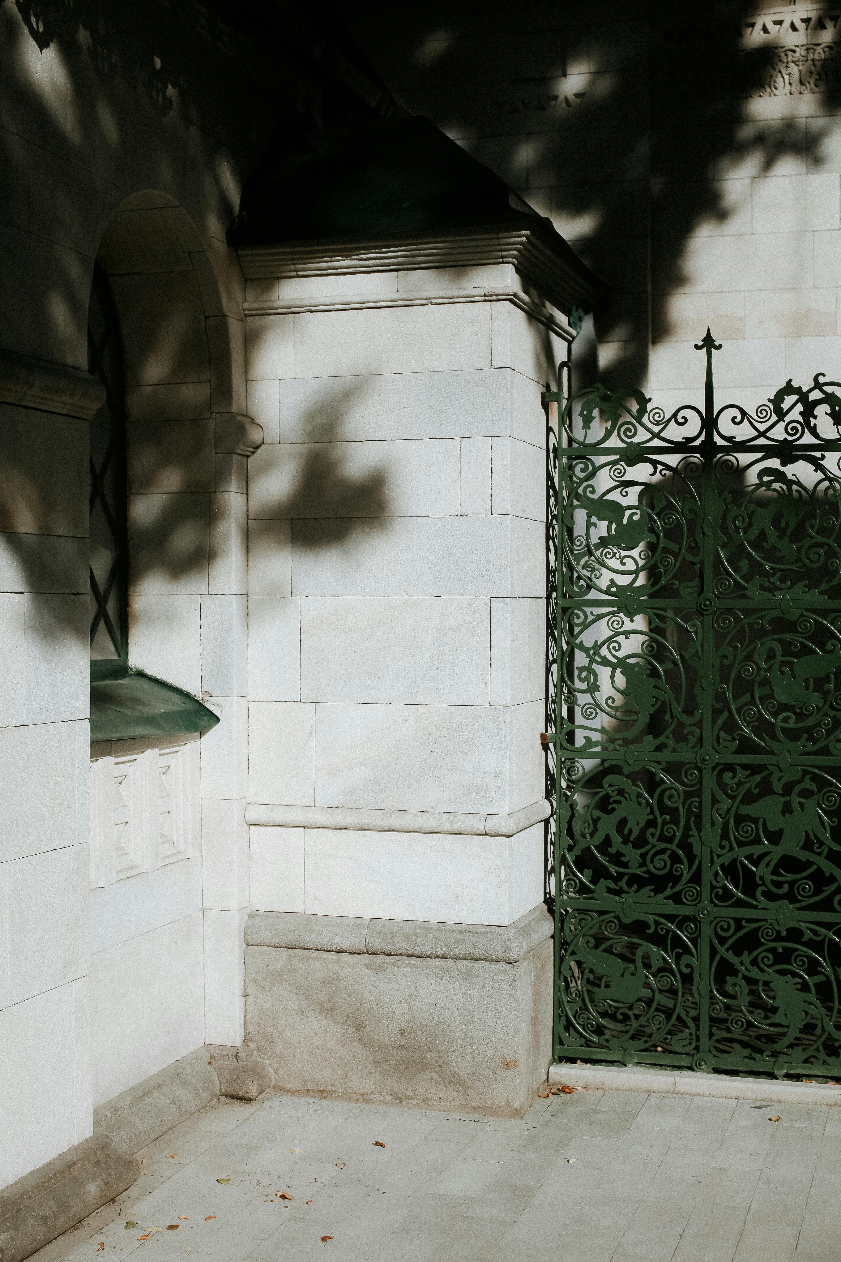 A beautifully ornate green gate casting shadows on an elegant stone wall in daylight.