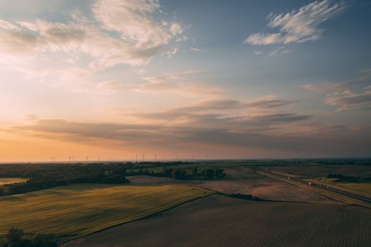 Serene aerial view of a sprawling farmland with a road, captured at sunset, under a sky of scattered clouds.