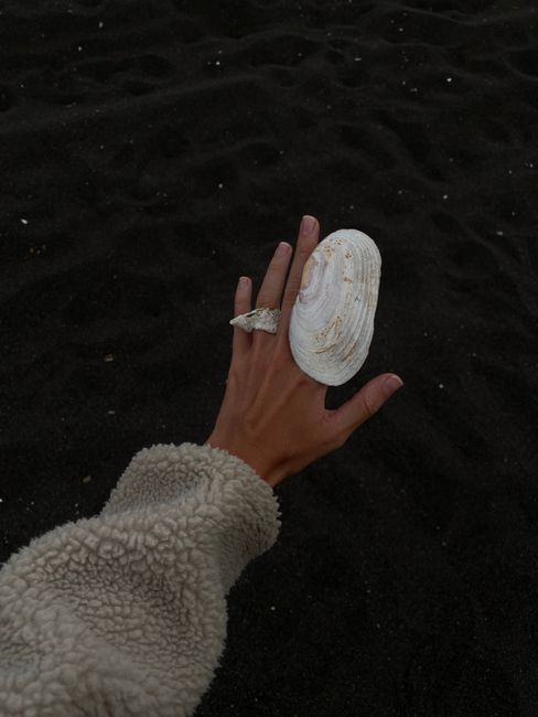 From above of crop unrecognizable female in warm wool jacket with creative seashell rings raising hand above rippling water