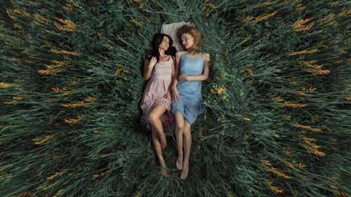 Free Two women in pastel dresses lying in a lush green field, captured from above. Stock Photo