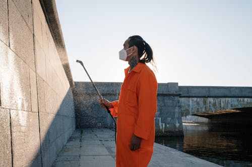 Woman in Orange Long Sleeve Shirt Standing Beside Concrete Wall