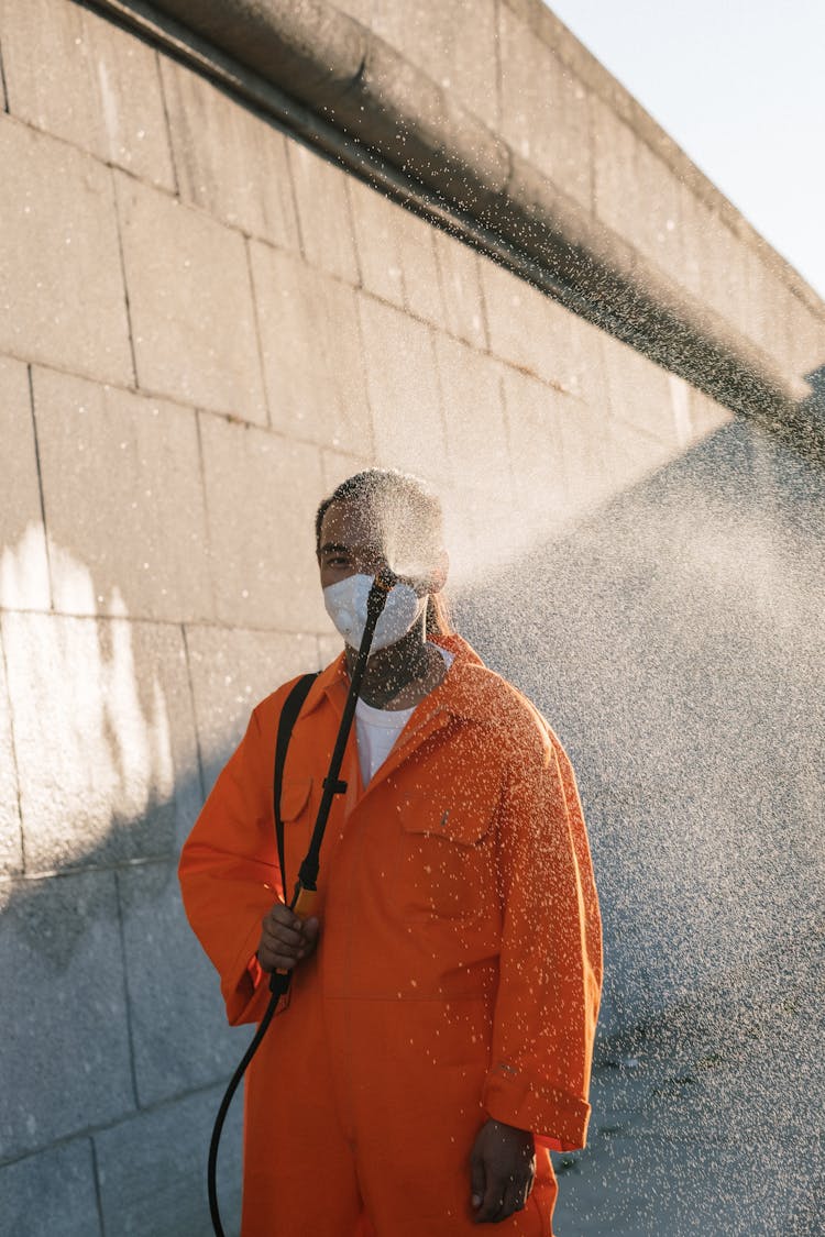 Man In Orange Jumpsuit Spraying Liquid Near A Wall