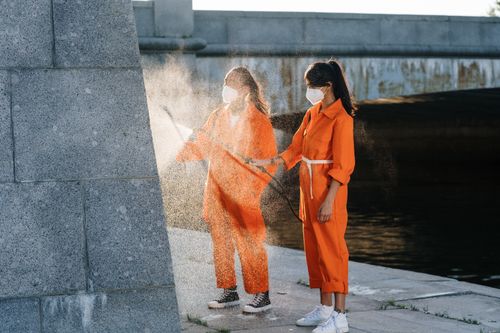 Free Two people in orange jumpsuits performing outdoor cleaning while wearing face masks. Stock Photo