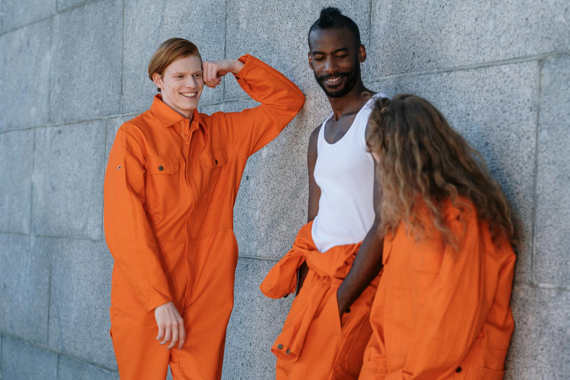 Adults in vibrant orange work uniforms converse and laugh against a concrete wall backdrop.