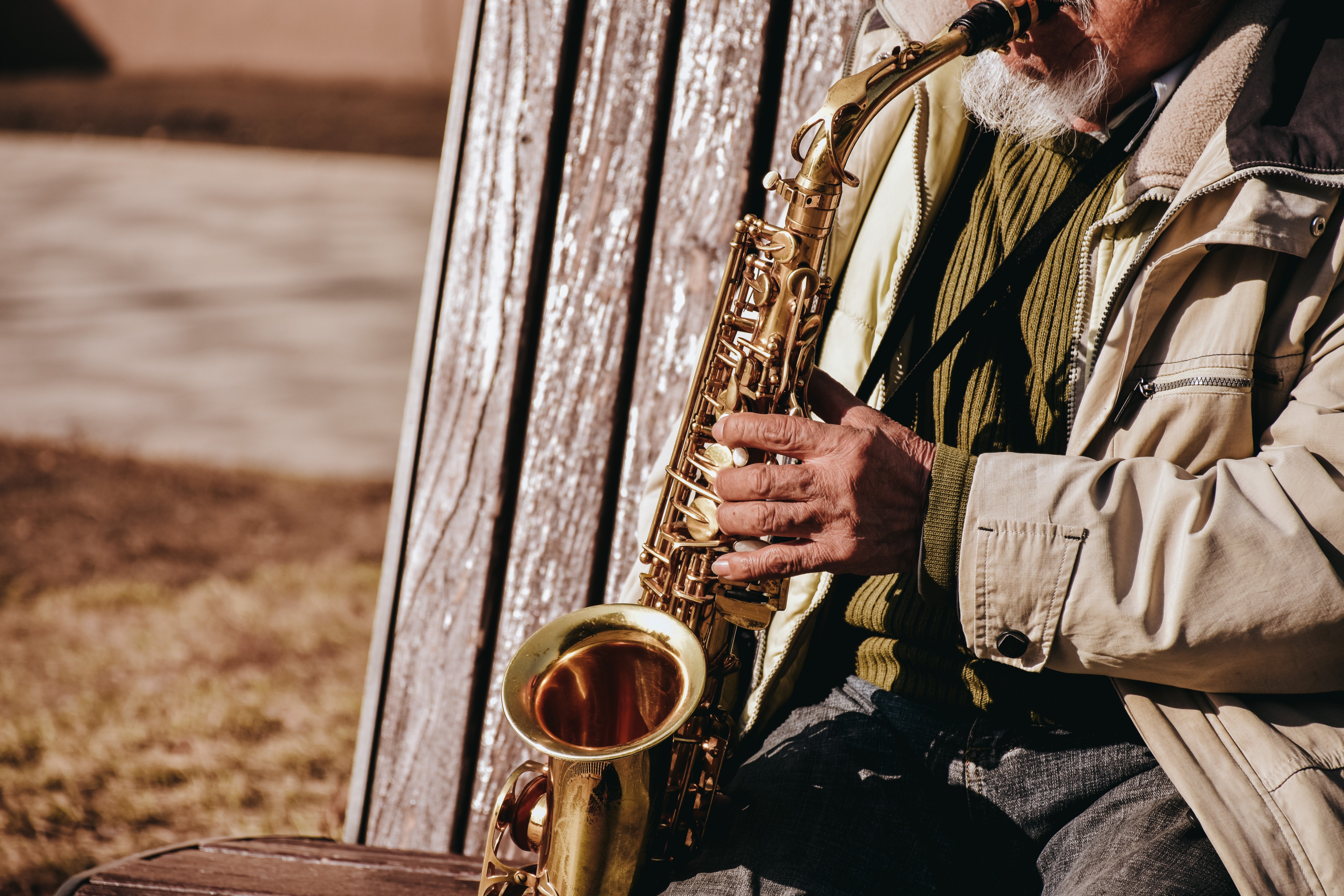 A senior adult playing the saxophone on a park bench, enjoying music outdoors.