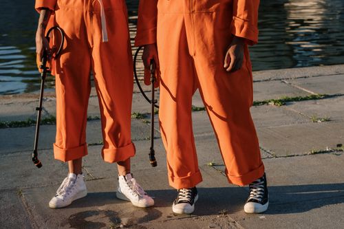Free Two individuals in orange jumpsuits holding sprayers on a concrete surface by the water. Stock Photo
