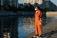Woman in Orange Coat Standing Near Body of Water