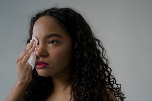 Free A thoughtful woman with curly hair wipes her eye using a tissue. Stock Photo