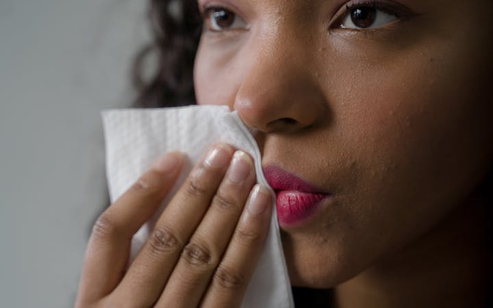 Close-up portrait of a woman gently removing lipstick with a tissue in a soft-lit indoor setting.