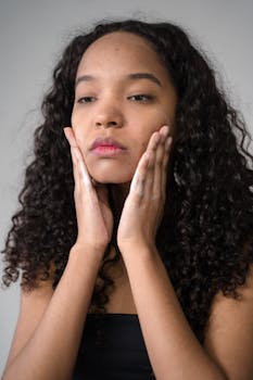A young woman with curly hair applies skincare products, focusing on her facial routine.