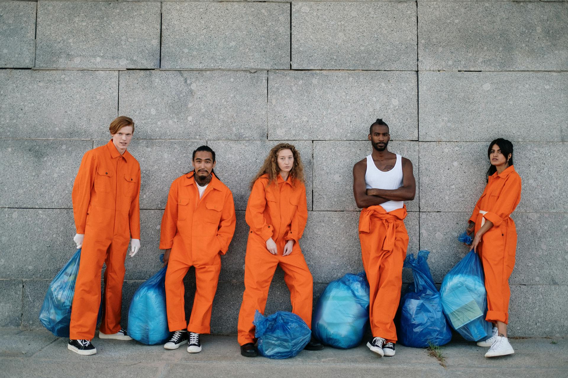 A Group of People Standing Beside Grey Wall with Blue Garbage Bag