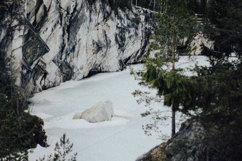 Free A peaceful winter scene with a rock formation beside a frozen lake, surrounded by trees. Stock Photo