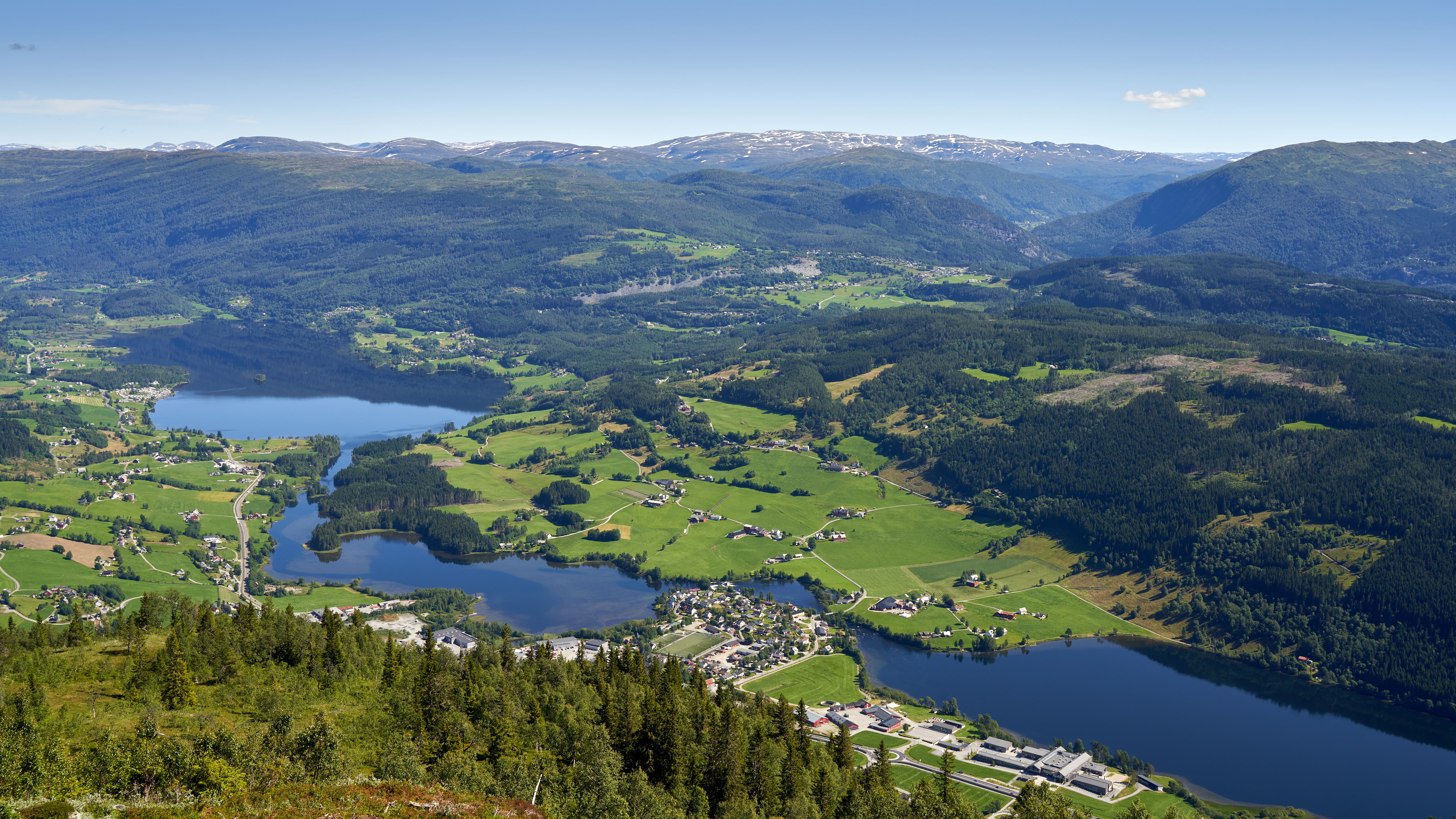 A stunning aerial view capturing a serene mountainous landscape with vibrant green fields and a reflective lake.