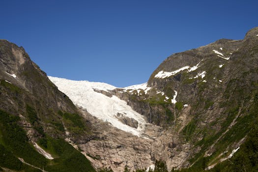 A stunning view of a glacier nestled between rocky mountains under a vibrant blue sky.