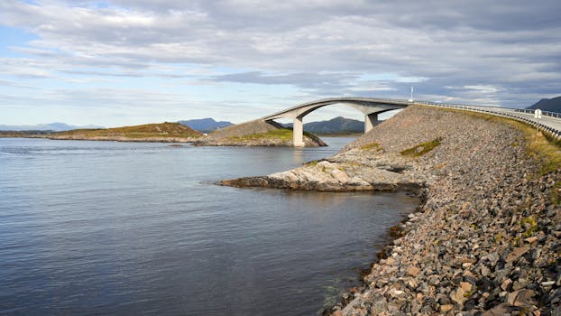 A picturesque bridge spanning a coastal waterway with rocky shores and distant mountains.