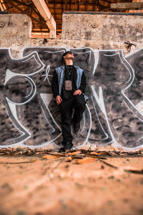 Free Young man in street fashion poses against a vibrant graffiti wall, embracing urban culture. Stock Photo