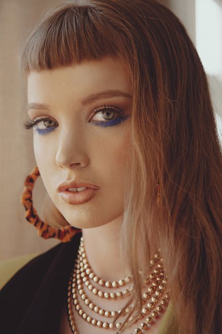 Close-up portrait featuring a woman with blue eye makeup and gold accessories, exuding elegance.