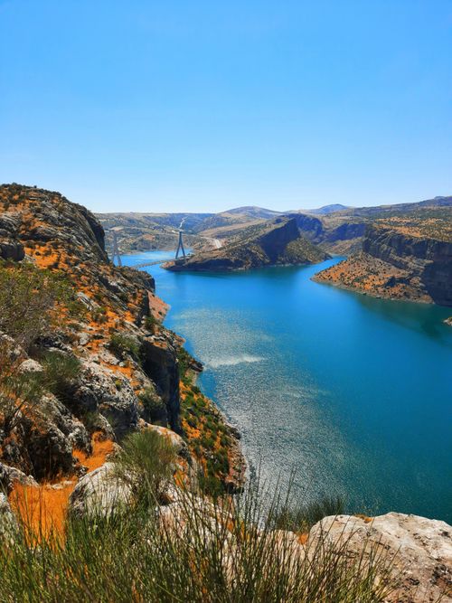 Free Stunning summer view of a vibrant blue bay surrounded by rocky cliffs and a bridge in the distance. Stock Photo