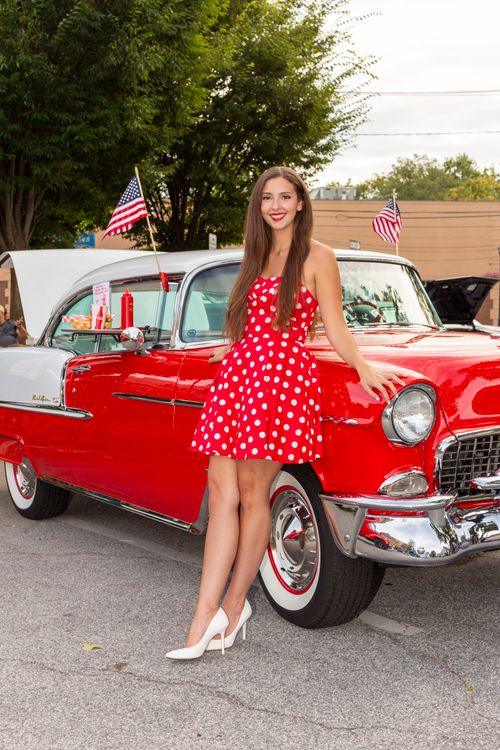 Free Woman in vintage dress poses with classic car at outdoor event, reflecting retro style. Stock Photo