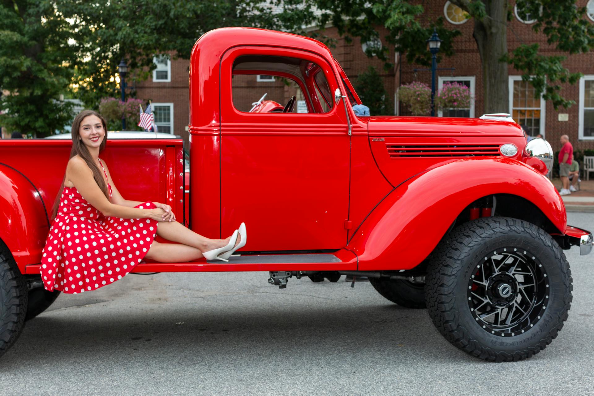 Smiling woman in polka dot dress sits on a classic red truck outdoors.