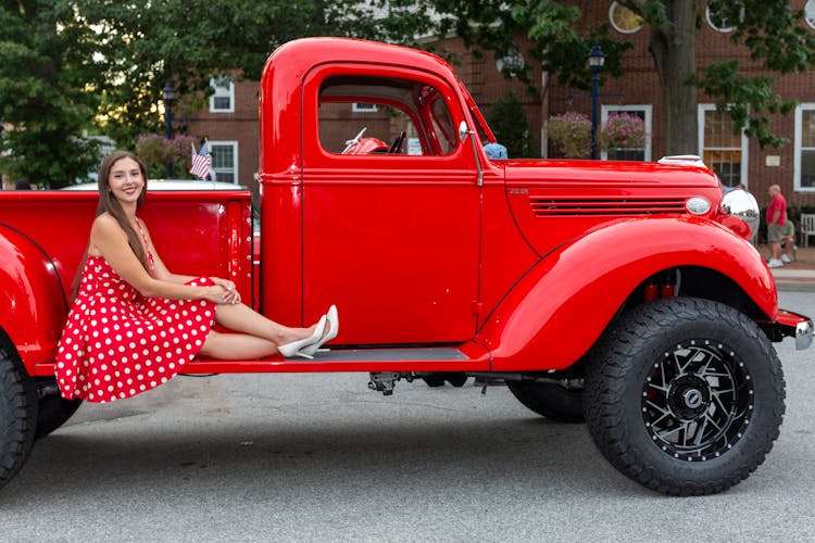 Woman In Polka Dot Dress Sitting On Red Vintage Pick Up Truck