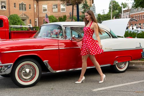 Free Stylish woman in a polka dot dress walking by a vintage red Chevrolet outdoors. Stock Photo