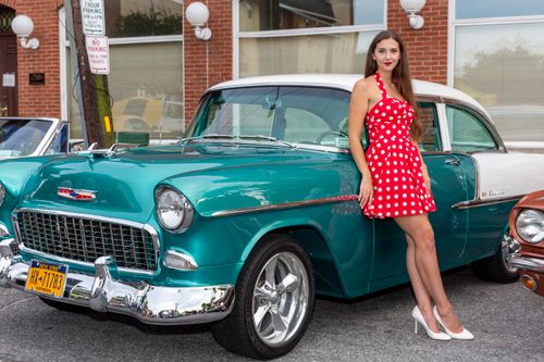 Free Woman in red polka dot dress leaning on classic Chevrolet in outdoor setting. Stock Photo