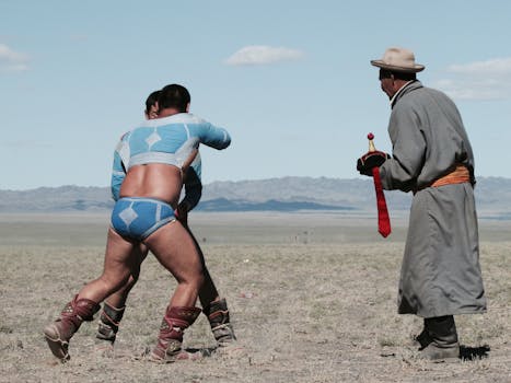 Two men in traditional attire wrestling outdoors with a referee nearby.