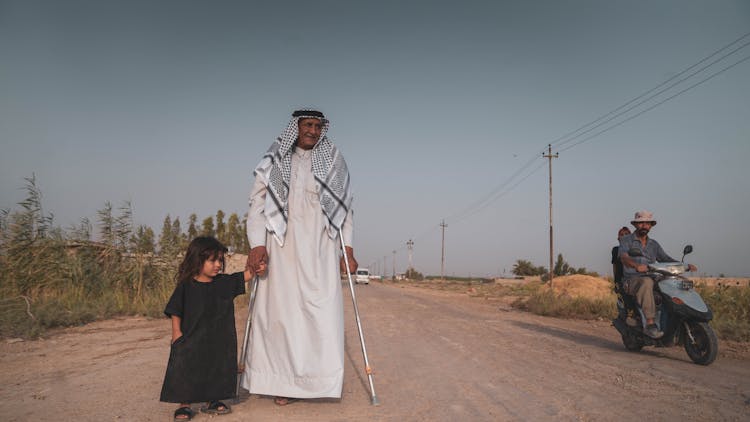 Senior Arab Man In Keffiyeh Holding Hand Of Little Girl In Long Black Dress