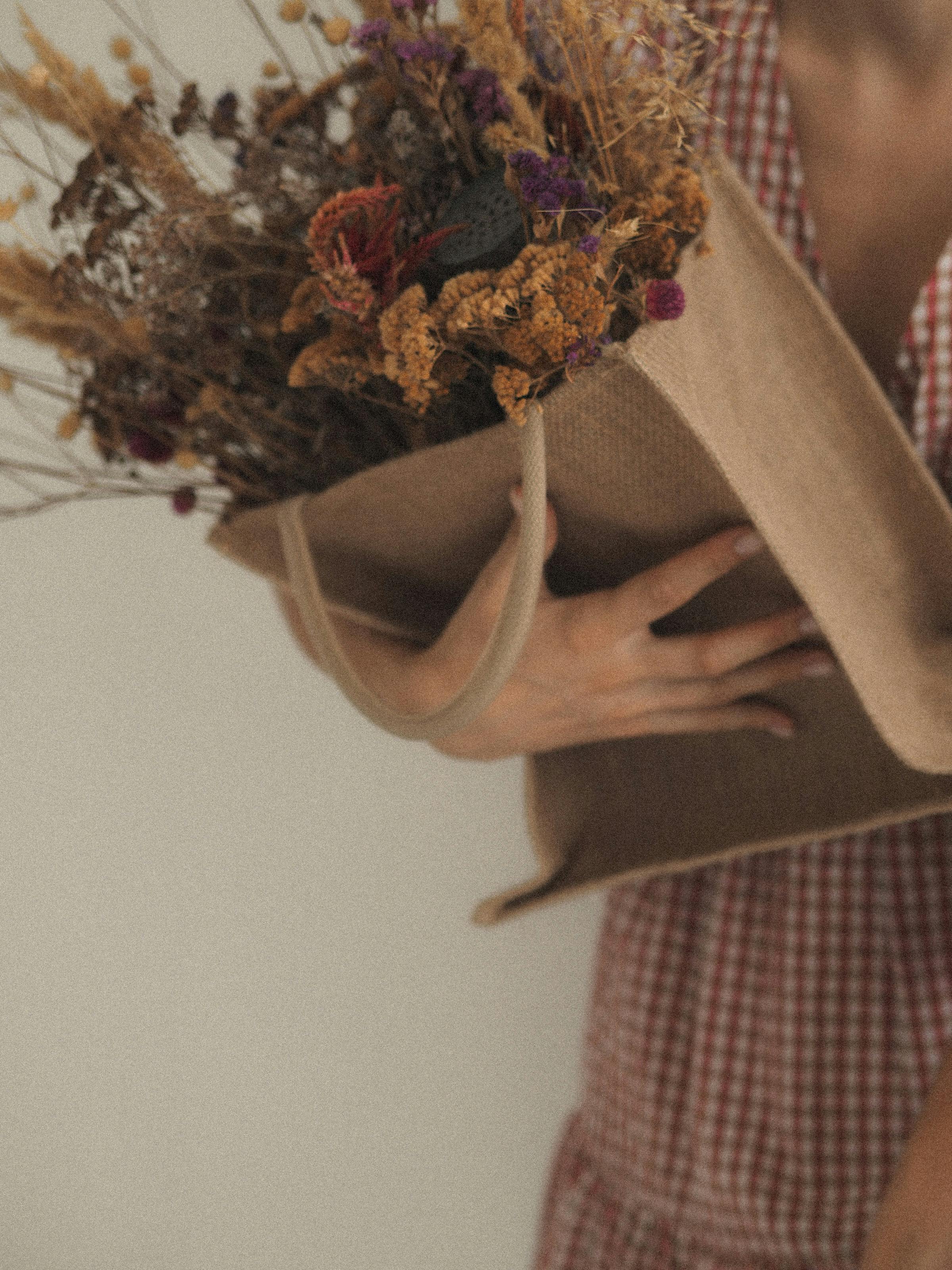 A woman in a plaid dress holding a bag of dry flowers against a white background for a rustic look.