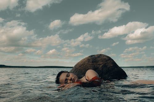 Free Woman Near a Rock Lying on Body of Water Stock Photo