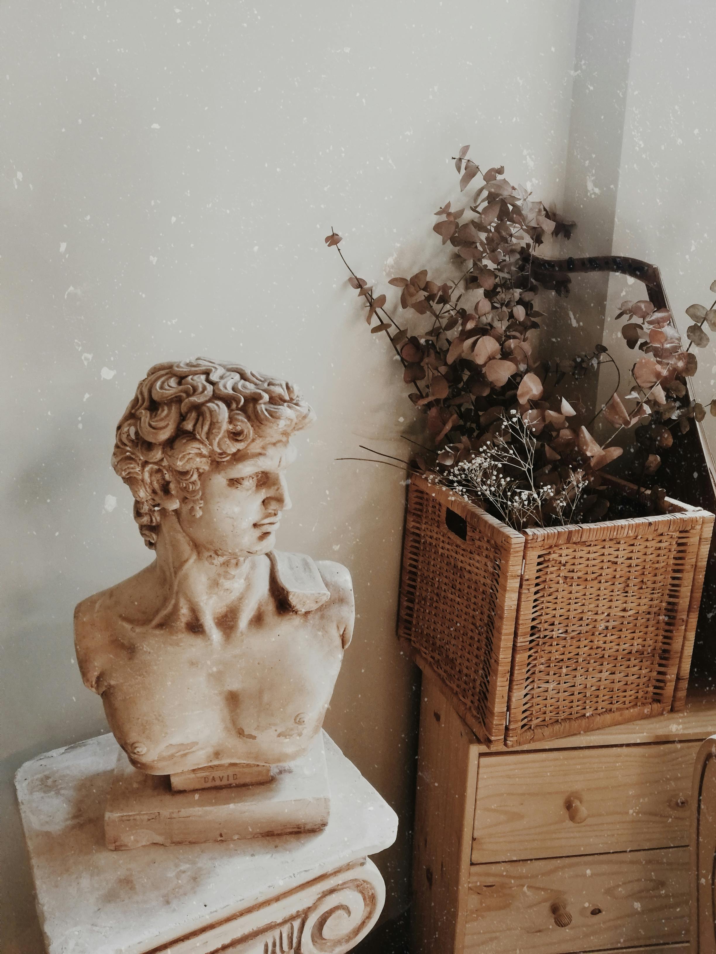 Classical bust on a pedestal with a rustic wicker box in a vintage-themed room.