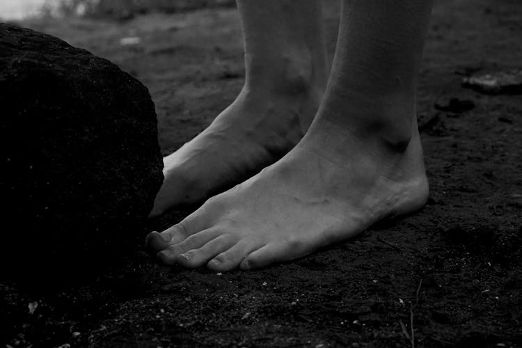 Bare Feet Of Person Standing At Boulder