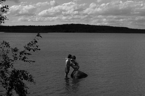 Woman Squatting on Rock in Water Kissing a Man