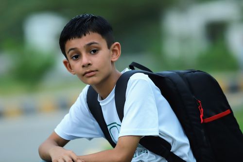 Free A young boy wearing a backpack looks at the camera in an outdoor setting. Ideal for back-to-school themes. Stock Photo
