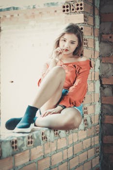 Stylish young woman posing outdoors in an urban brick wall setting, showcasing fashion and attitude.
