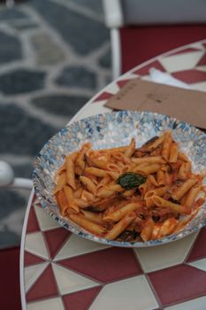 A mouthwatering bowl of penne pasta in tomato sauce served on a mosaic table outdoors.