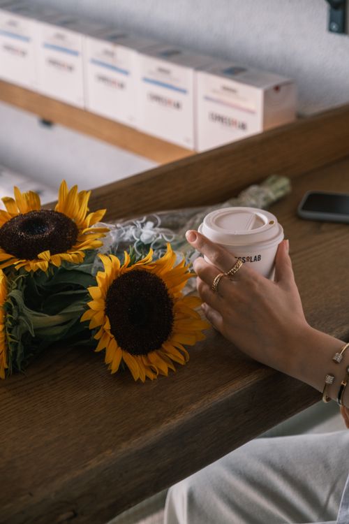 Free A floral bouquet of sunflowers beside a disposable coffee cup held by a woman. Stock Photo